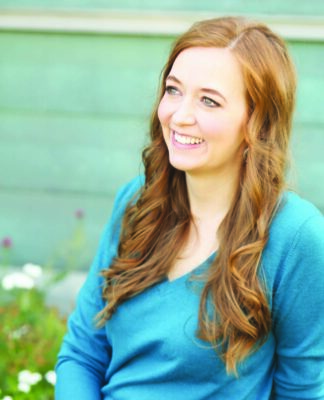 young woman with long hair, wearing blue shirt, sitting outside, smiling