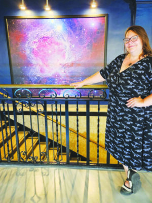 Woman standing in front of picture of galaxy above a staircase