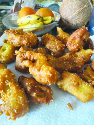 small fried bananas beside bowl of bananas and oranges, and a coconut