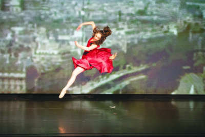 female dancer in red dress, leaping in air in dance studio