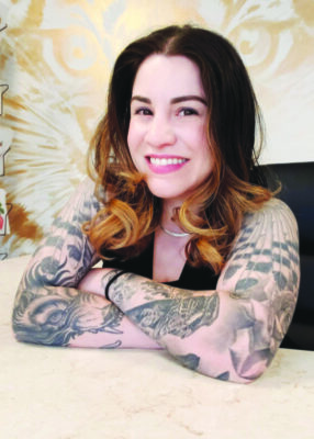 Young woman with dark hair and tattooed arms smiling at the camera
