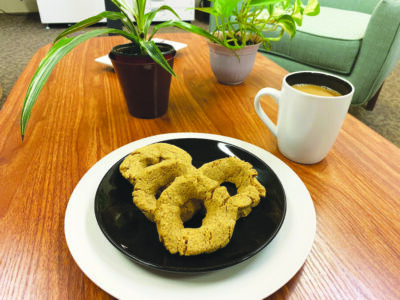 ring shaped biscuits on plate on table beside mug of coffee and 2 potted plants