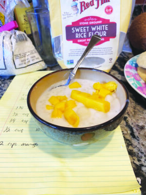 bowl of light colored pudding topped with pieces of mango, on counter beside ingredients