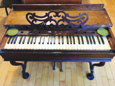 melodean that looks lie a small piano, made of wood, decorative sheet music stand attached to top