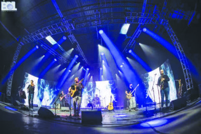 fish eye photo of band on stage with screens in background and blue lights 
