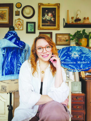woman wearing glasses, with long hair, sitting in room with small paintings on wall