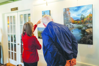 an elder man and woman looking at paintings on a wall in a gallery