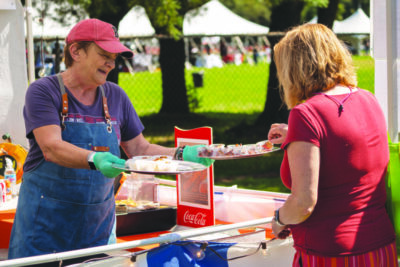woman handing festival goer a sample on sunny day at outdoor food festival