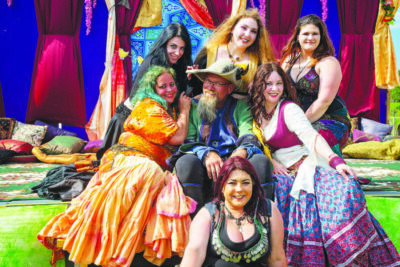women dressed medieval fantasy bodices and long colorful skirts, posing on dancing stage with bearded man