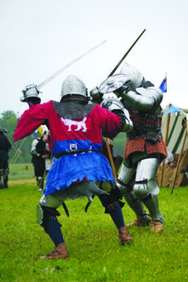 2 men on field, dressed in armor and tunics, fighting with swords