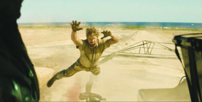 Ryan Gosling or his stunt double leaping toward the camera above desert landscape in action shot from movie