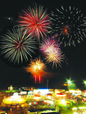 fireworks over a brightly lit fair on a field