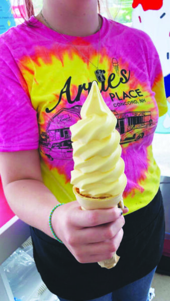 woman shown from neck down wearing tie dye t-shirt holding tall soft serve ice cream cone