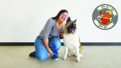 young woman kneeling beside happy dog, posing for photo in front of gray wall with pup in a cup logo on wall