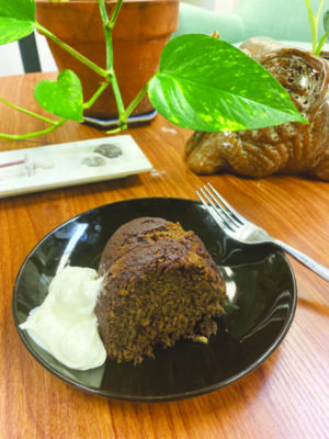 piece of chocolate bundt cake on plate with cream on the side and fork