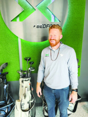 man standing in front of row of golf bags, against wall with company logo