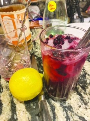 dark red daquiri in tall glass with blueberries on counter beside lemon