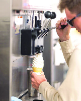 man holding ice cream cone under soft serve machine while twisting the soft serve ice cream