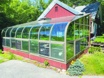 greenhouse attached to farmhouse with seedlings inside on sunny day