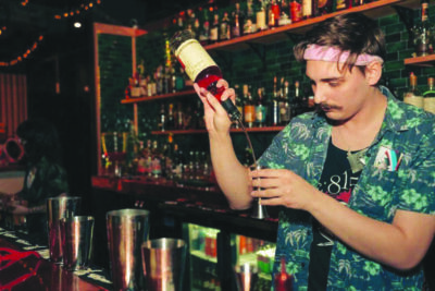 young man at bar pouring alcohol into cocktail shaker