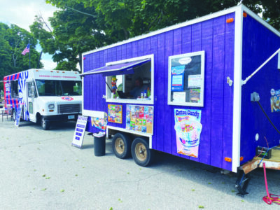 purple food truck with signs on the side parked in front of another food truck pained in red and blue