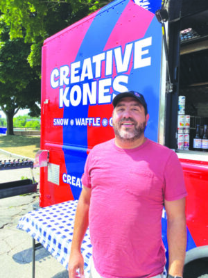 man wearing baseball cap standing in front of red and blue painted food truck on sunny day, words creative kones on side of truck