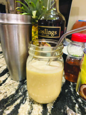 cocktail in mason jar with metal straw, sitting on a counter beside bottles of ingredients