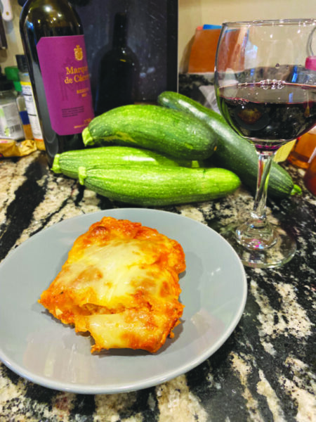 piece of zucchini parmesan sitting on plate on counter with glass of wine