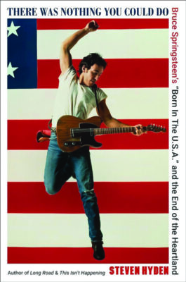 Man jumping playing guitar with the American flag in the background