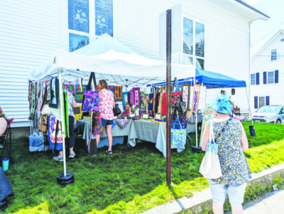 pop up canopy set up on lawn beside building, containing crafts for sale