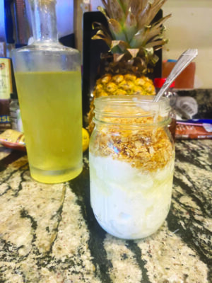 mason jar filled with yogurt and topped with granola, on counter beside bottle with cucumber syrup