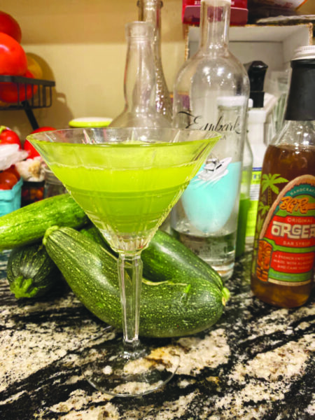 martini glass filled with green cocktail sitting on counter beside zucchini