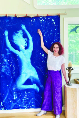 woman standing in front of painted wall hanging of figure dancing, abstract star motif