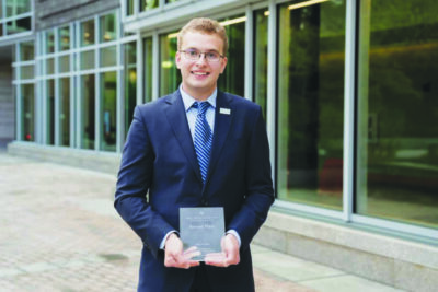 young man standing outside of building holding small plaque