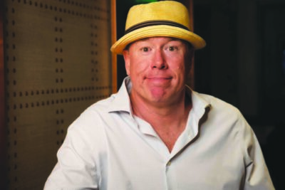 headshot of middle aged man with small smile, wearing brimmed hat and button up shirt