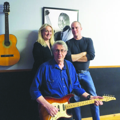 man sitting and holding guitar, woman and another man standing behind him