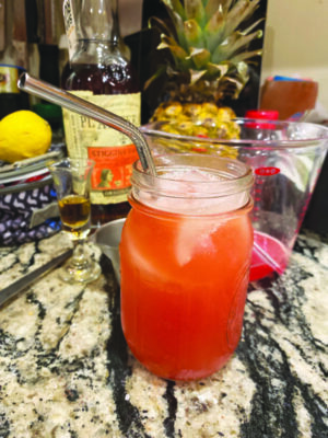 mason jar with reddish orange cocktail with ice, metal straw sticking out, on marble counter