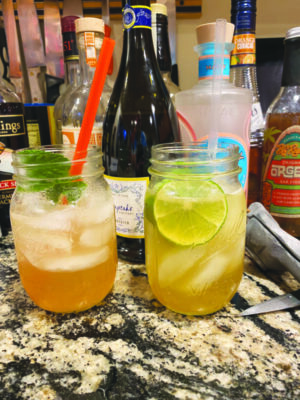 two mason jars with cocktails with ice, one with lime garnish and one with mint garnish