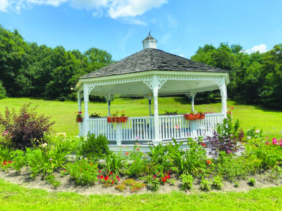 a gazebo on a large grassy lawn, surrounded by a garden of colorful flowers, sunny day