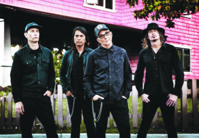 4 men posing in front of old building, dark clothing, serious expressions