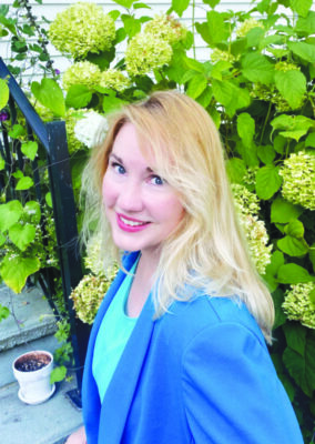 Woman with blond hair wearing blue blue and dark blue jacket smiling at the camera