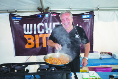 Man standing over portable stove, cooking in large pan during demonstration in tent