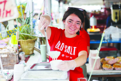 young woman ladling chowder into a cardboard bowl under tent at food festival