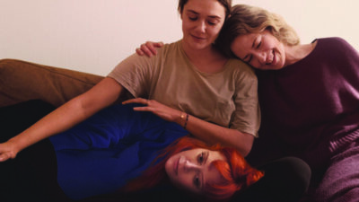 screenshot from movie His Three Daughters showing three women embracing each other on a couch