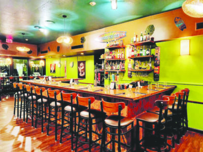 inside of restaurant with painted green walls, bar against wall with tall chairs lining it outside, fun colorful atmosphere