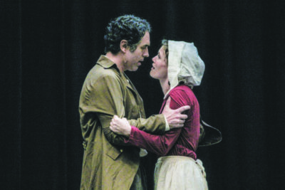 man and woman in colonial costume, on stage with black background, holding onto eachother during intense scene