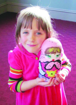 little girl wearing pink dress happily holding up her painted nesting doll also done in pink color scheme