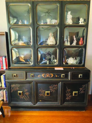 dining room cabinet painted dark brown with lighter brown designs painted on doors, figurines behind glass on shelves