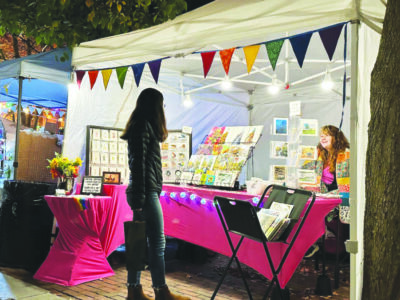 woman standing in front of booth at art fair, at night