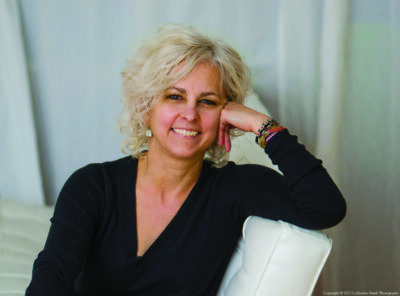 mature women with short light hair wearing black shirt, posing on chair, leaning head against one hand, smiling